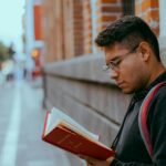 Rahul S Young man reading a red book on a city street. Focused and engaged in an urban setting.
